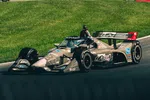 IndyCar race car speeding on track with grass background, featuring sponsor logos and aerodynamic design.