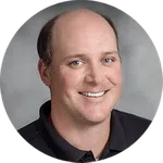 Portrait of a smiling bald man wearing a black polo shirt against a gray background
