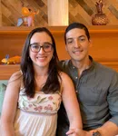 Smiling young couple sitting closely with decorative wooden shelves and colorful animal sculptures behind them