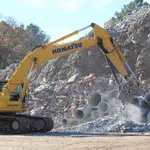 Komatsu PC360 LC excavator handling concrete debris and pipes at a construction excavation site in daylight.