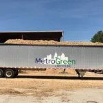 Metal trailer loaded with wood chips parked outside a recycling facility under blue sky.