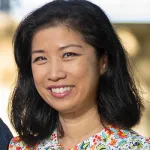 Smiling Asian woman with black hair wearing a floral patterned top in bright natural light