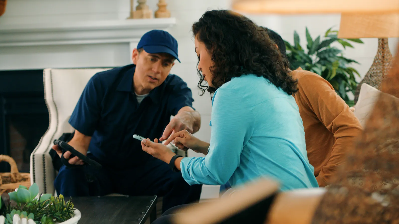Technician in blue uniform instructs woman on device use during home service visit in living room.