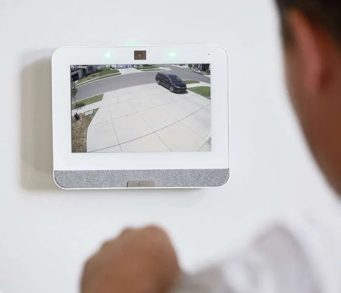 Home security monitor displaying front driveway and parked black car viewed by person indoors.