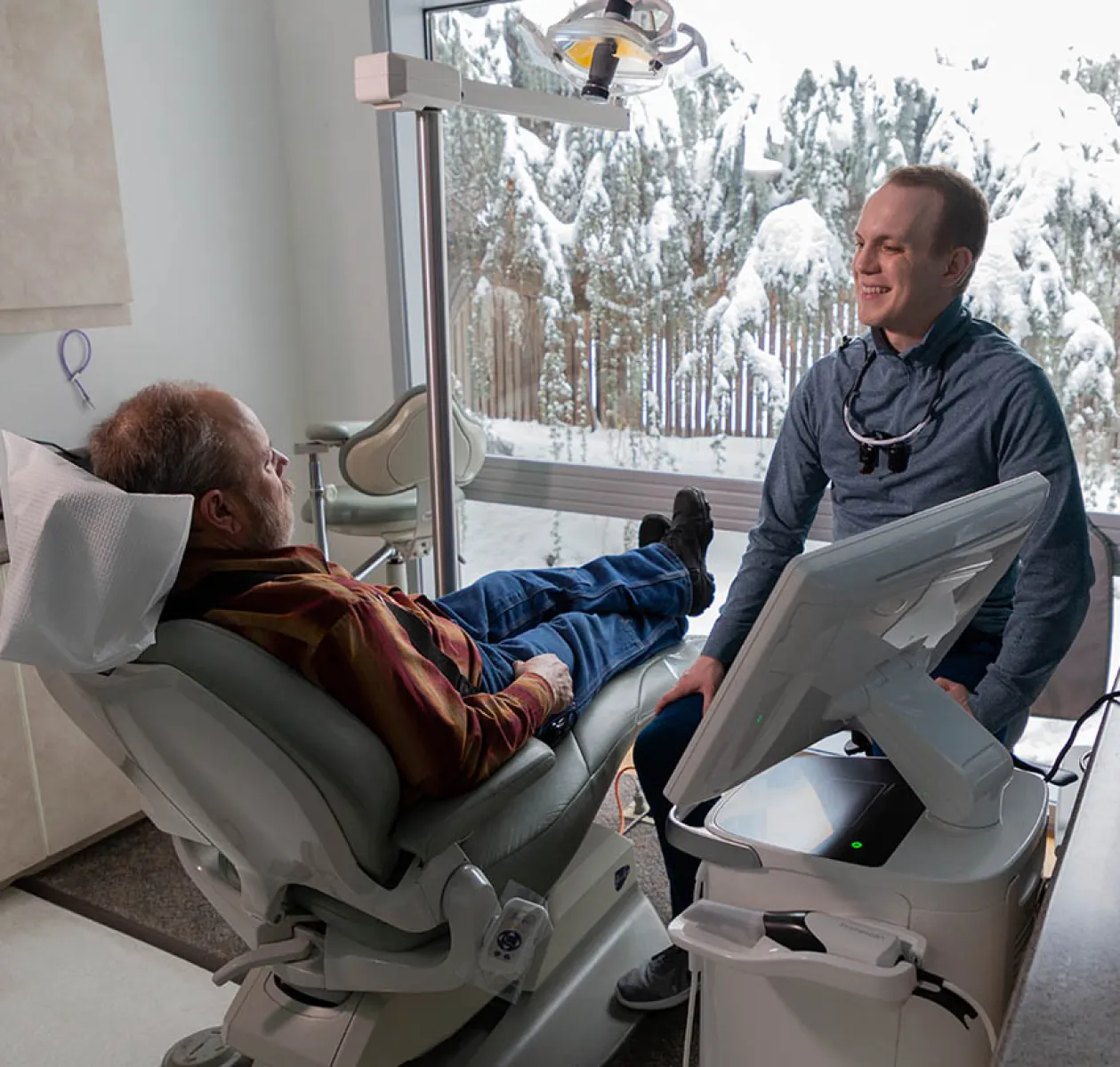 Dentist consulting with a patient in a modern office with snowy trees visible through large windows.