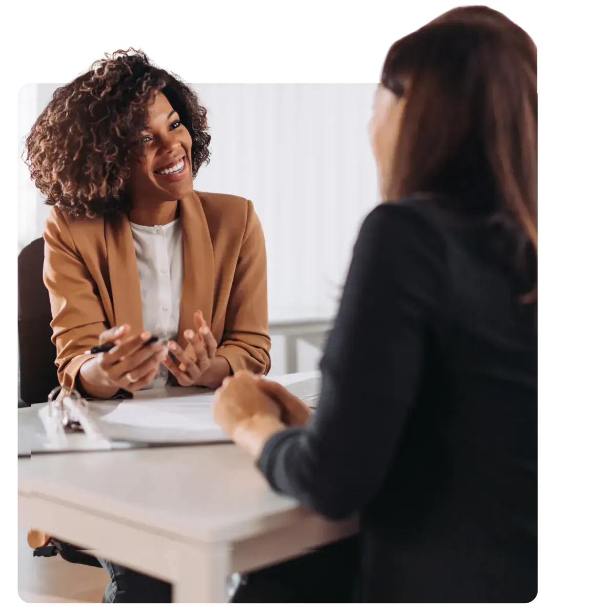Two professional women engaging in a positive business meeting at a desk with documents and a clipboard