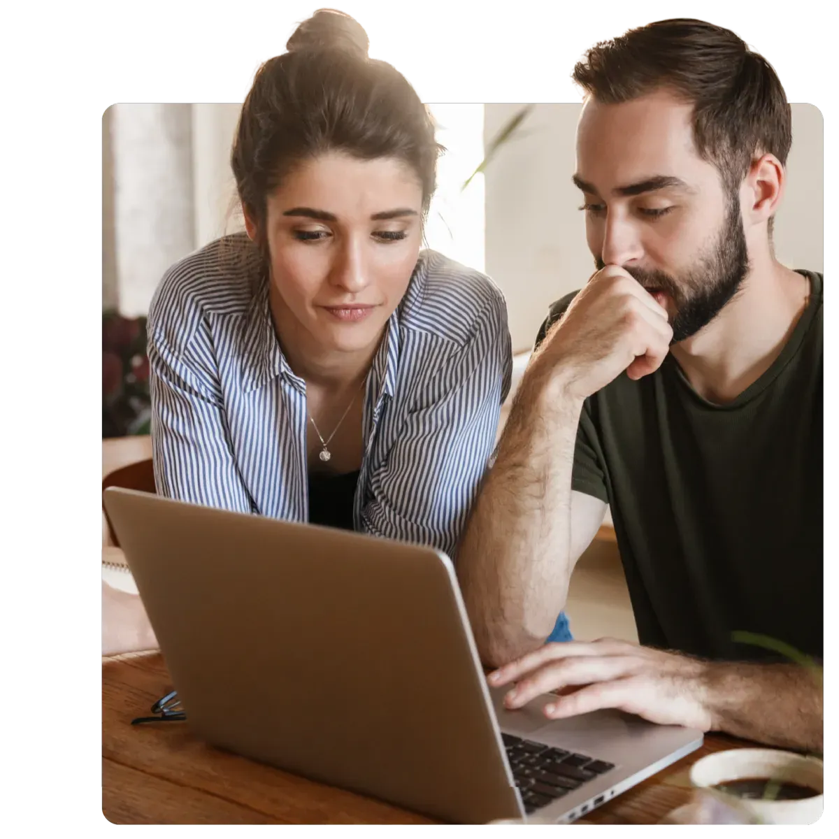Young man and woman focused on laptop screen while working together at wooden table indoors