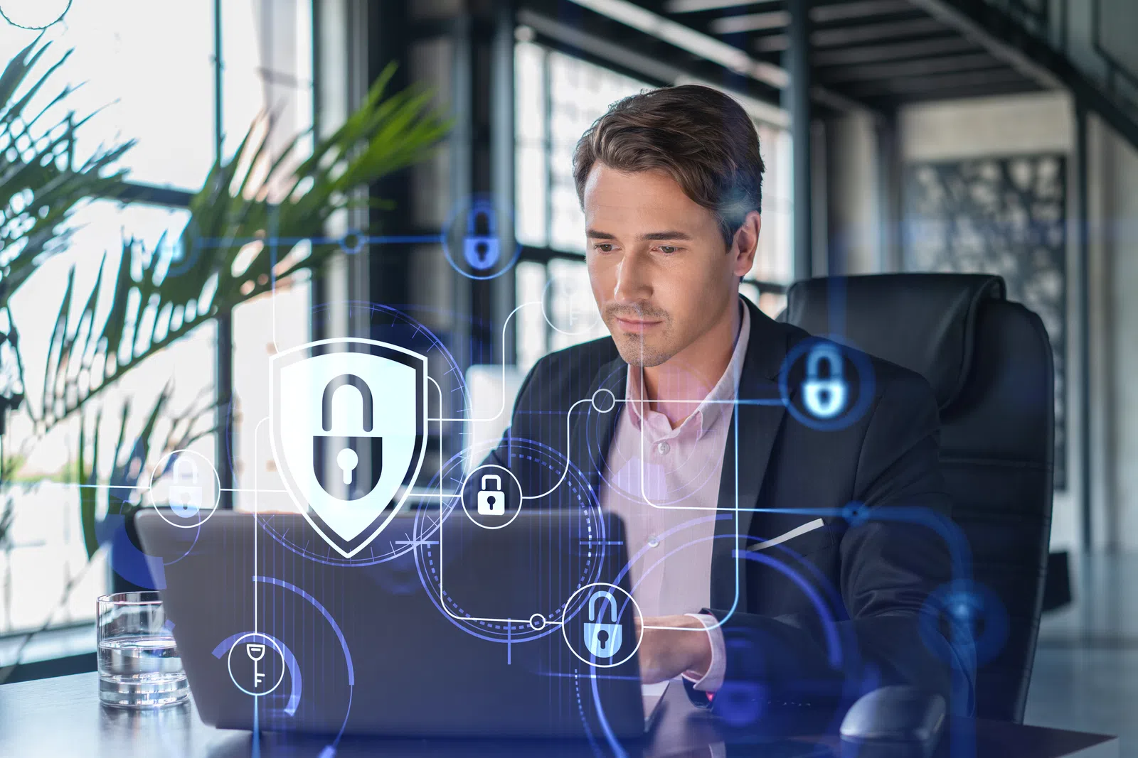 Businessman working on laptop with cybersecurity shield and lock icons overlay in modern office environment.