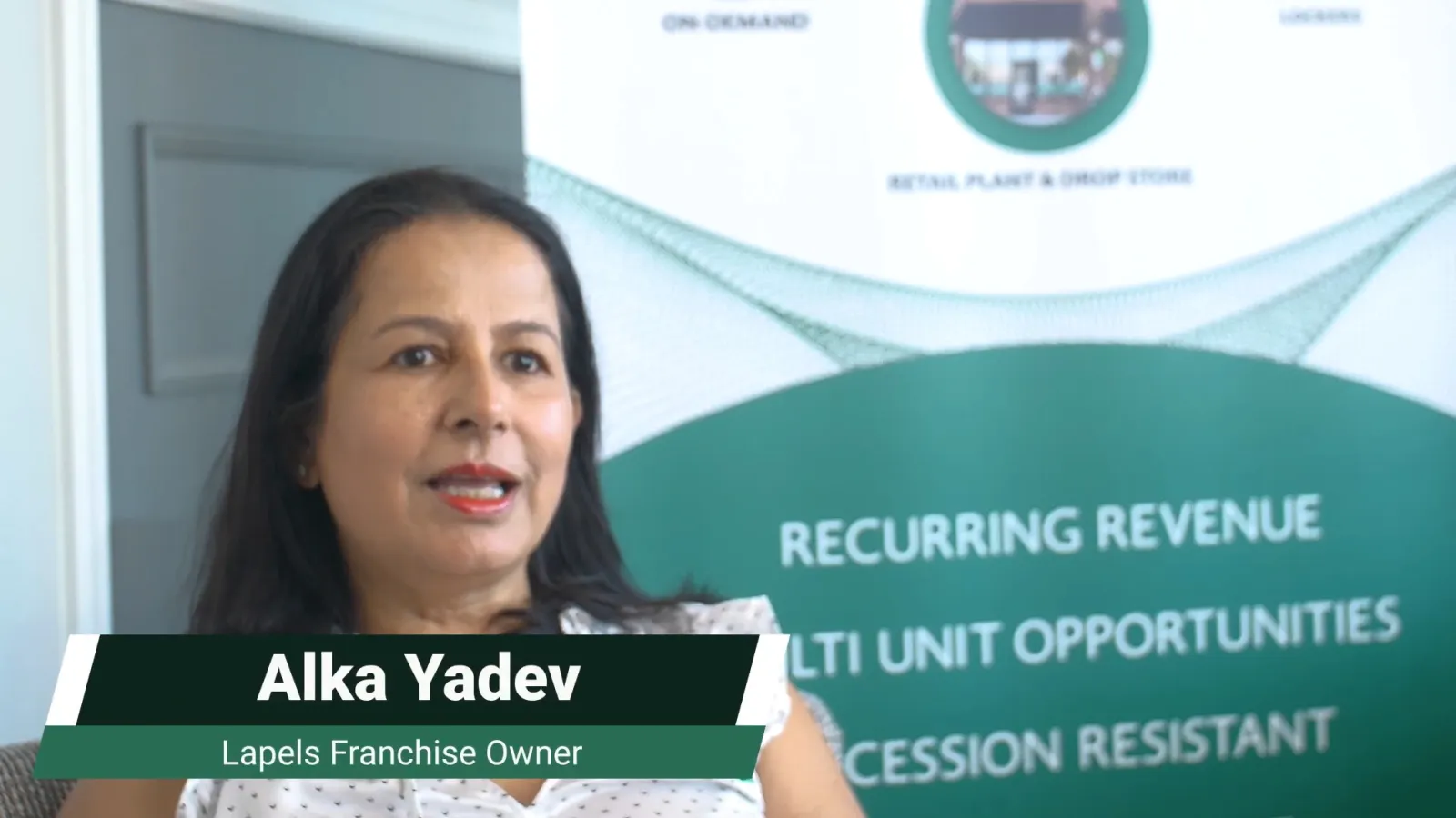Alka Yadev, Lapels Franchise Owner, speaking with a banner listing business benefits behind her.