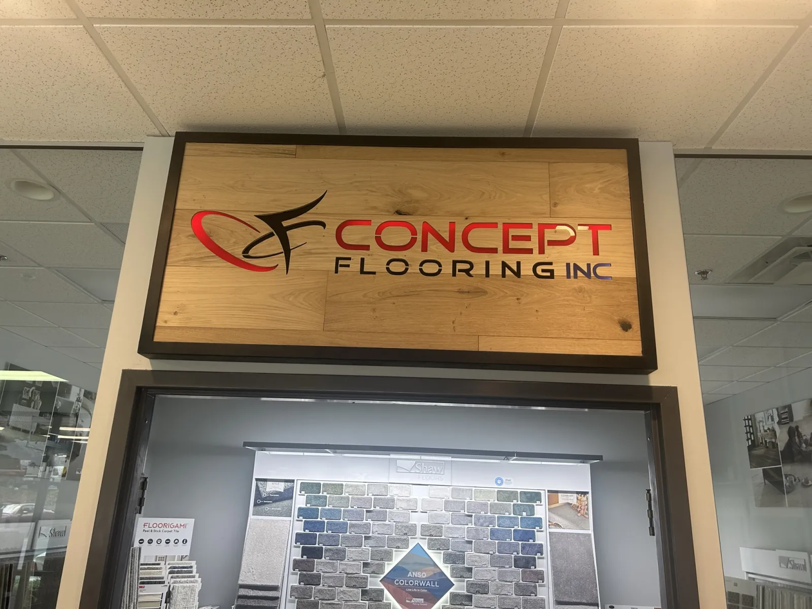 Wooden sign for Concept Flooring Inc above a showroom displaying various flooring samples and color options.