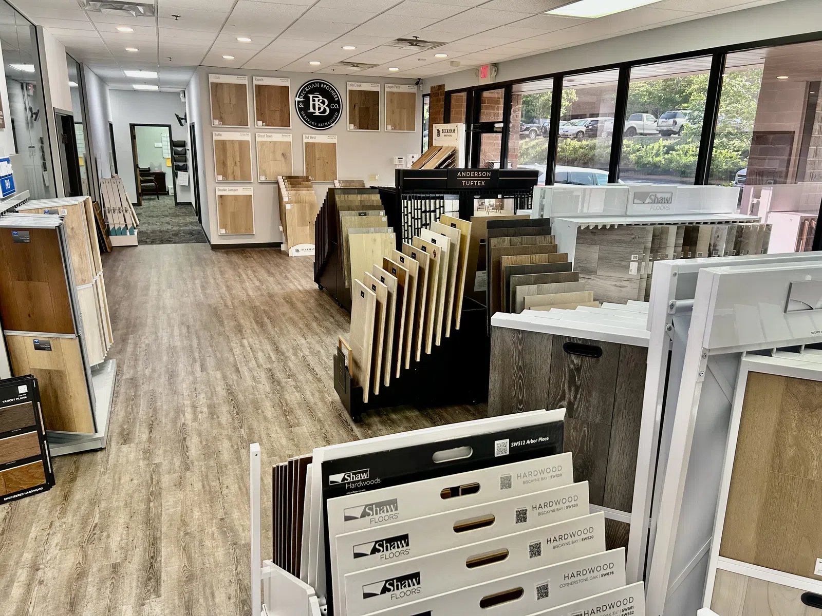 Flooring showroom displaying various hardwood floor samples on stands and walls with large windows letting in natural light.