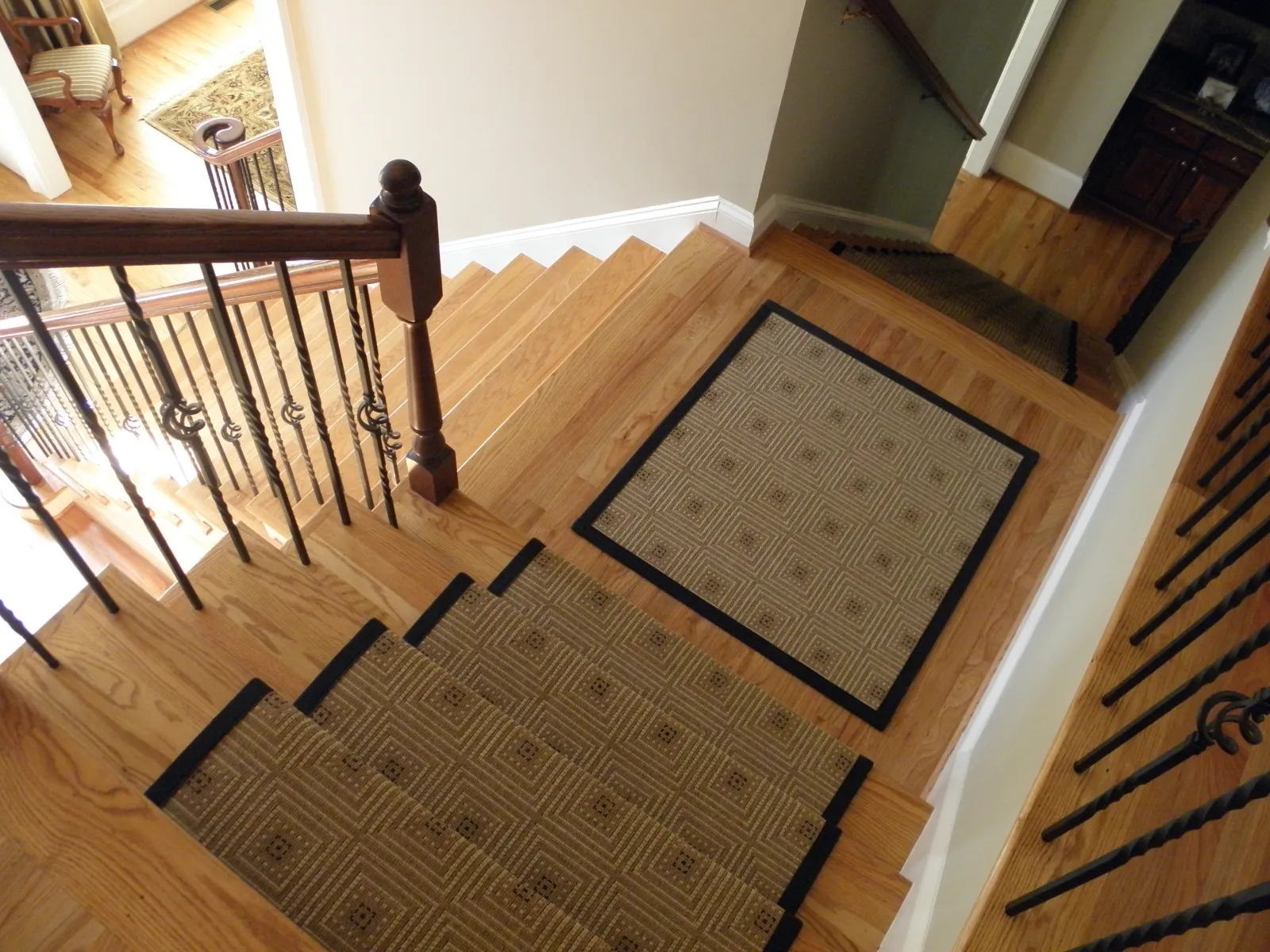 Wooden staircase with patterned brown carpet runners and black metal railings in a home interior