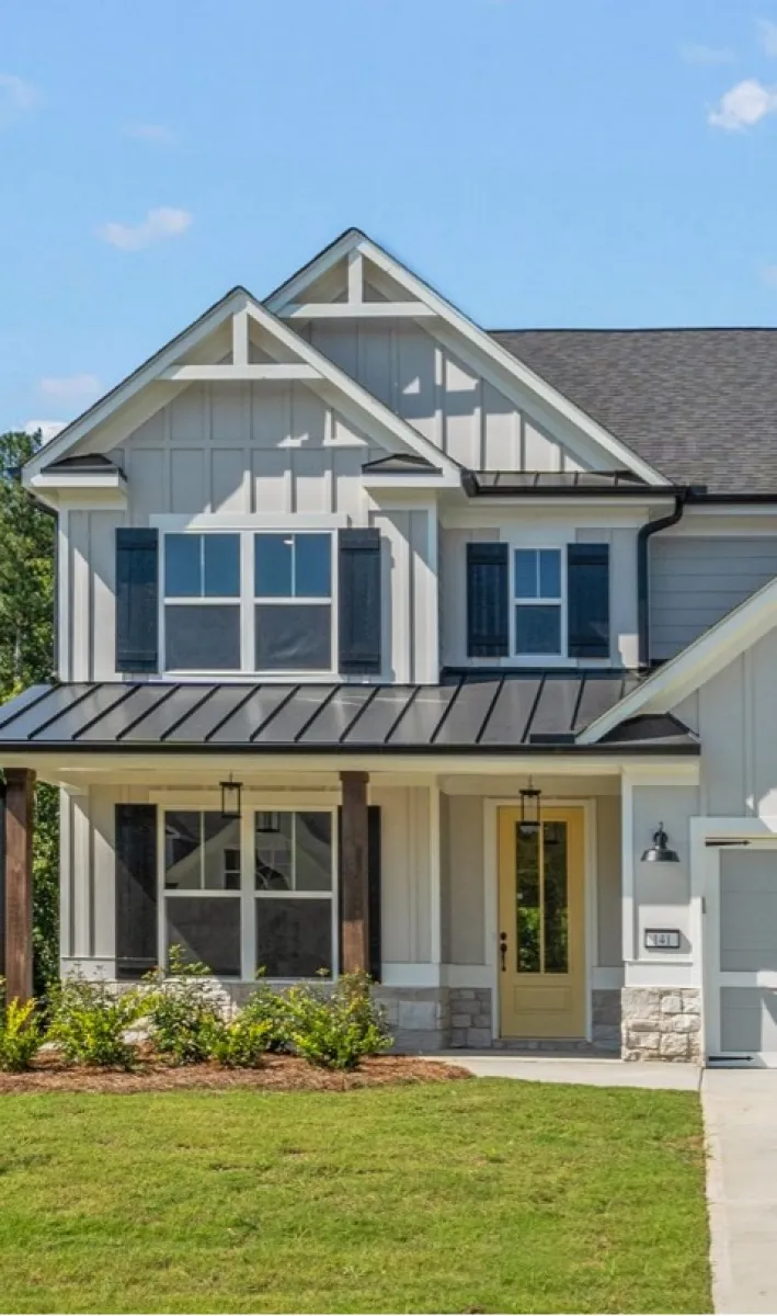 Modern two-story house with beige siding, black shutters, yellow front door, and manicured lawn under blue sky