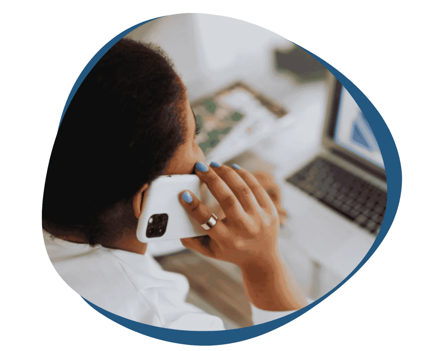 Person with blue nail polish holding a smartphone to ear while looking at a laptop screen.