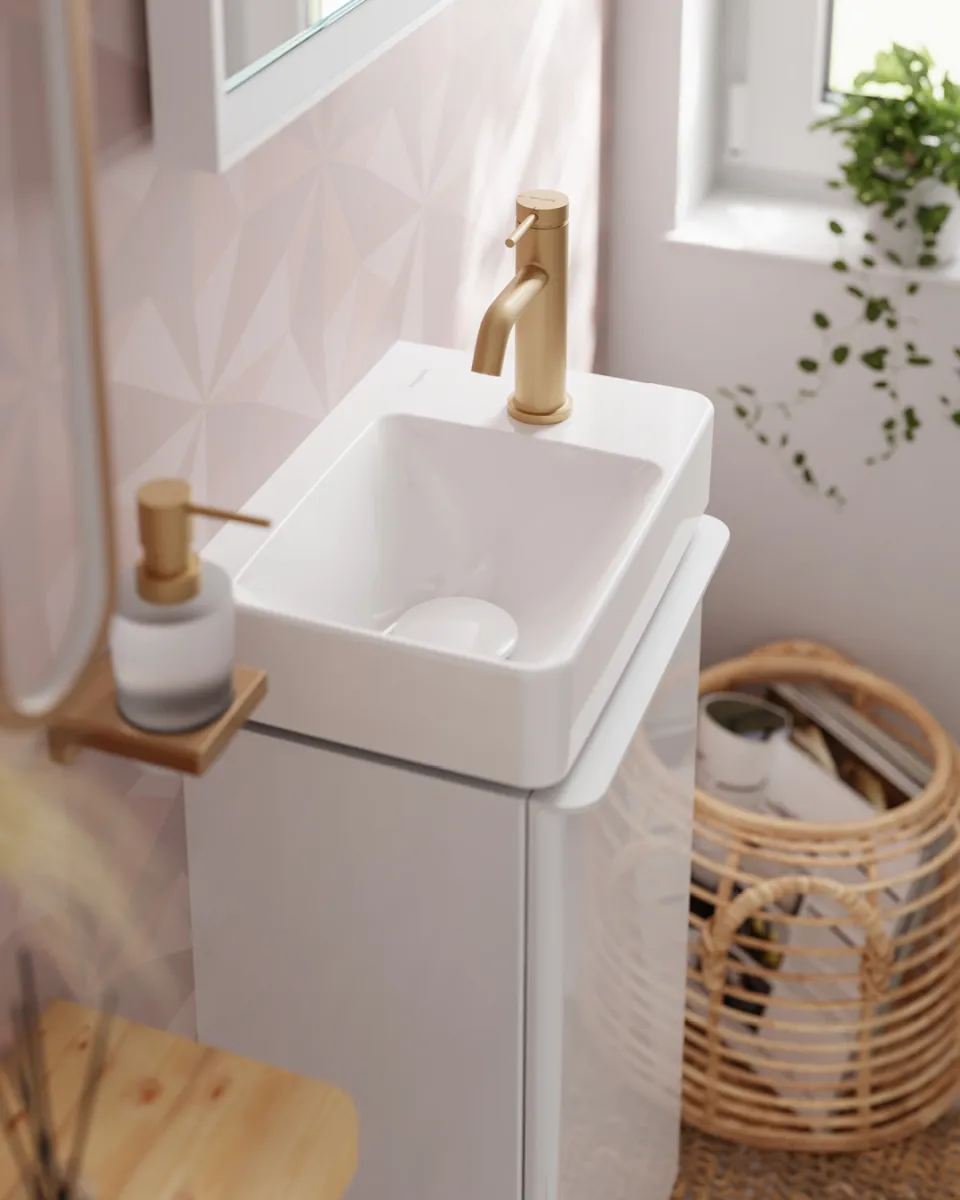 Modern white bathroom sink with gold faucet, soap dispenser, geometric wall tiles, and woven basket nearby.