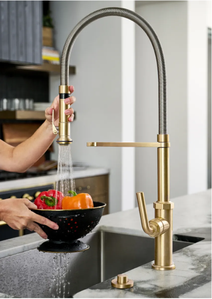 Modern gold kitchen faucet with flexible spout washing colorful bell peppers in black colander.