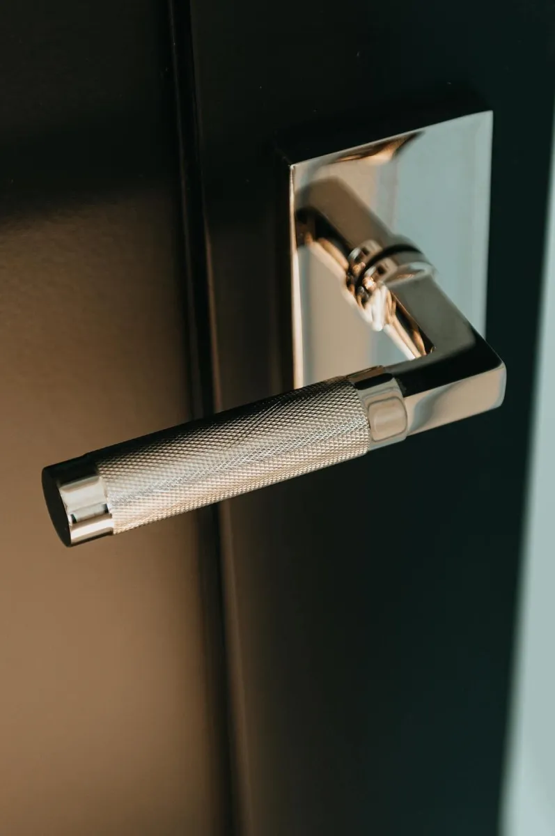 Close-up of a modern textured silver door handle on a black door with a reflective metal base plate.