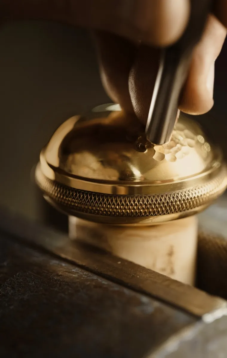 Close-up of hand engraving intricate patterns onto a shiny golden metal surface with engraving tool.