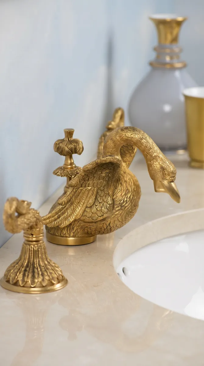Elegant gold swan-shaped faucet and matching handles on marble bathroom sink countertop.
