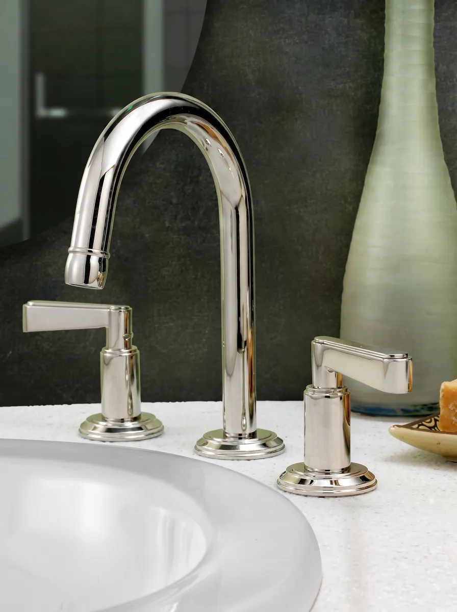 Modern chrome bathroom faucet and handles mounted on a white countertop with a textured dark background.