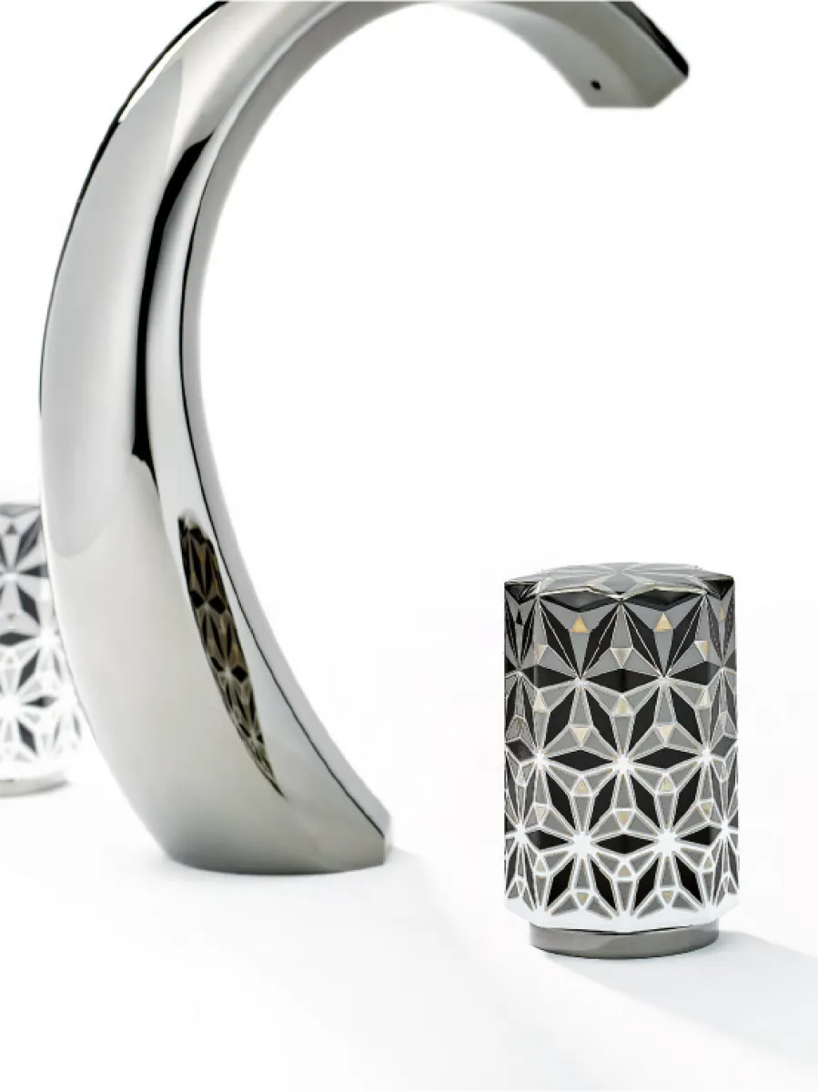 Polished chrome faucet handle with intricate geometric pattern against white background.