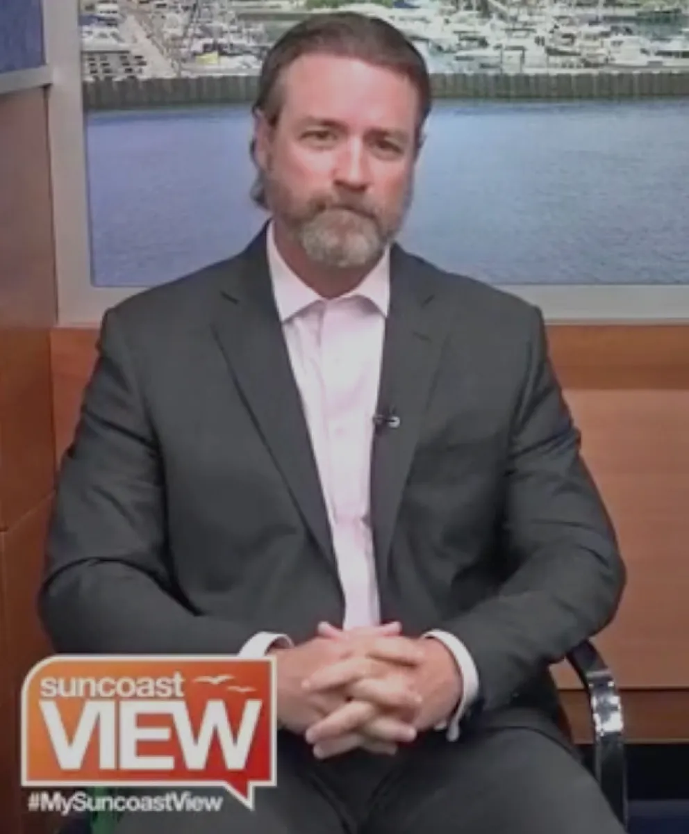 Man in dark suit with beard sitting in studio with marina backdrop on Suncoast View show interview