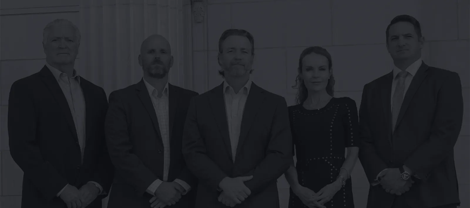 Five professionally dressed individuals standing in front of a building with columns, posing confidently for a group photo