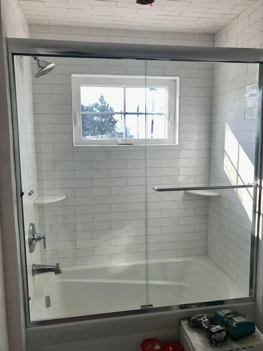 Modern bathroom with white subway tile tub surround, glass shower doors, and window above tub.