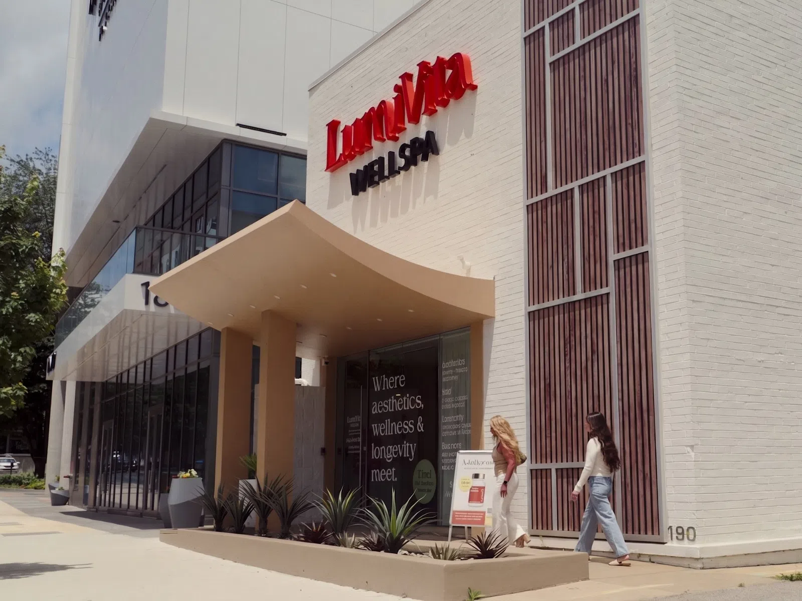 Two women walking toward LumiVan Med Spa entrance with modern white building and red signage