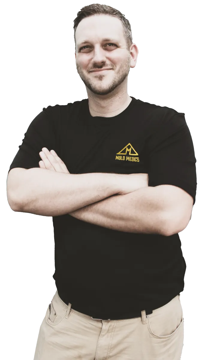 Man with crossed arms wearing a black Mold Medics shirt and tan pants smiling confidently
