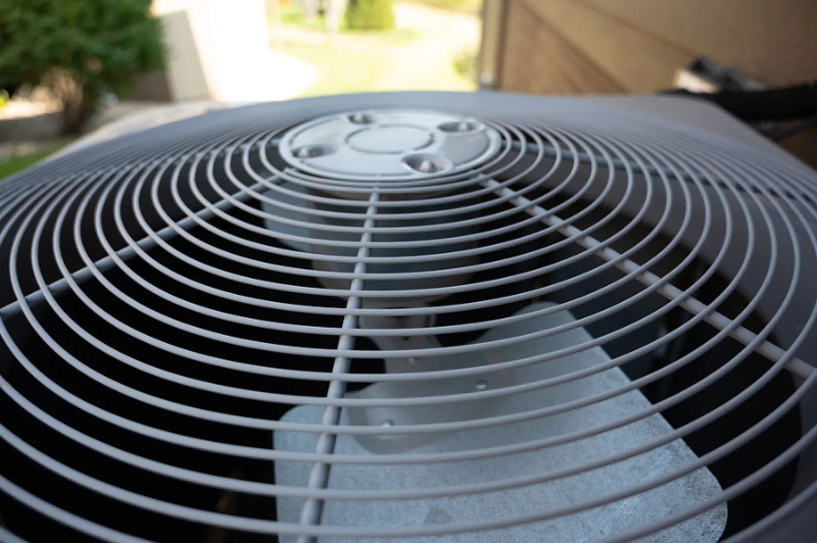 Top view of an outdoor air conditioning unit showing the protective grille and fan blades in sunlight.