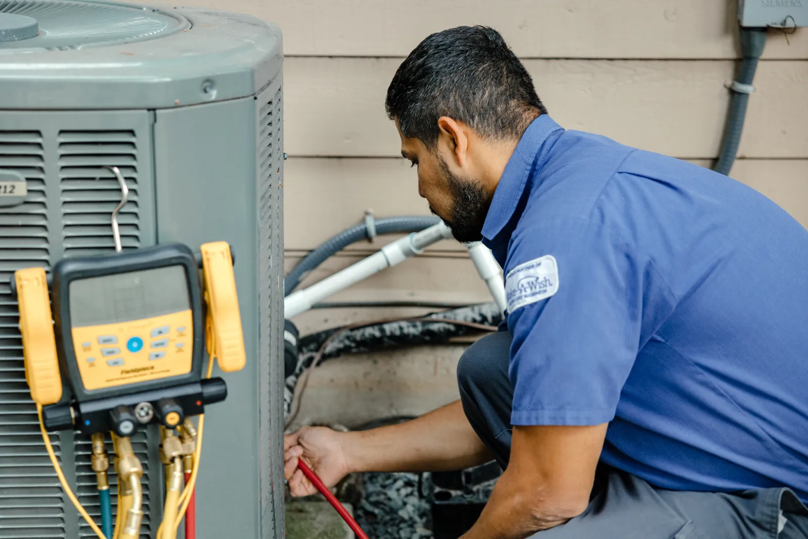 Technician in blue uniform inspecting and repairing residential air conditioning unit with diagnostic tools