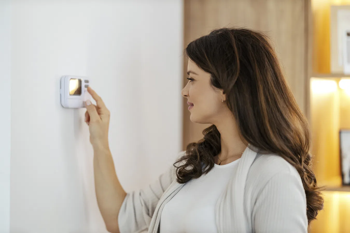 Woman adjusting a digital thermostat on a wall in a modern home, managing indoor temperature settings