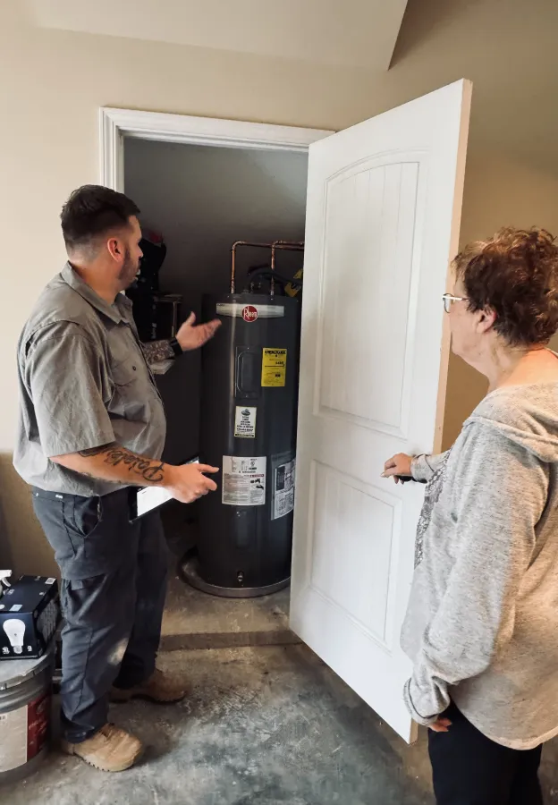 Technician explaining a water heater installation to a homeowner in a utility closet at home.