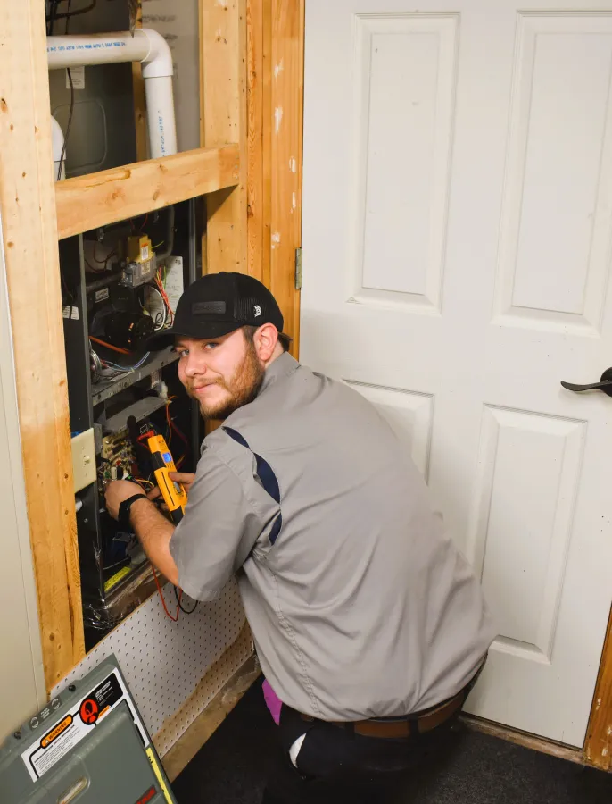 Electrician working on a circuit panel in a home, wearing a cap and focused on the task.