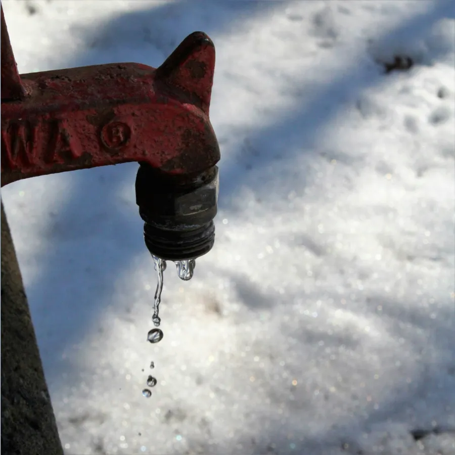Rusty outdoor faucet dripping water with frozen snow background on a cold winter day