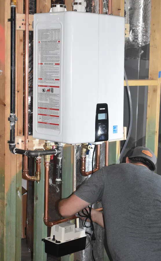 A technician installs a tankless water heater, showing pipes and tools in a well-lit workshop.