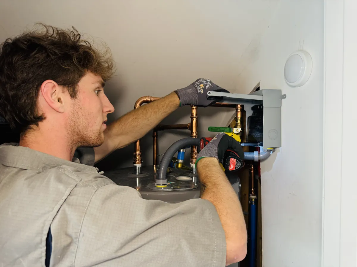Technician in gray shirt and gloves repairing water heater.