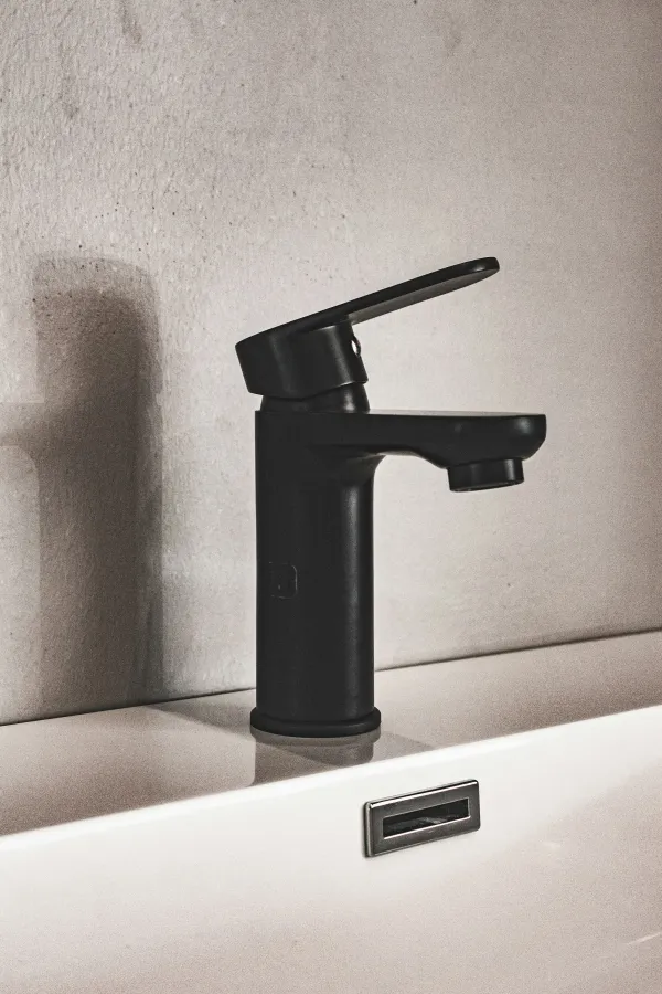 Modern matte black faucet mounted on a white sink against a textured beige wall with soft shadow.
