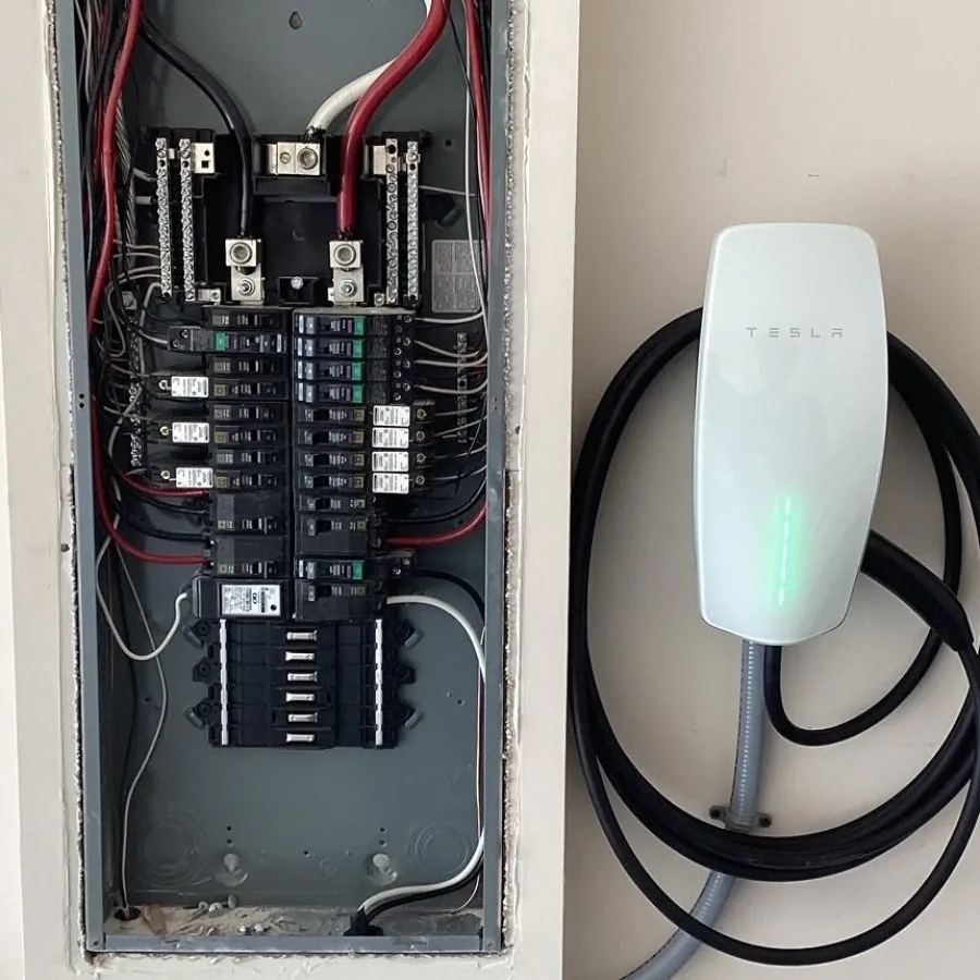 Tesla home charging station installed next to a circuit breaker panel for electric vehicle charging.