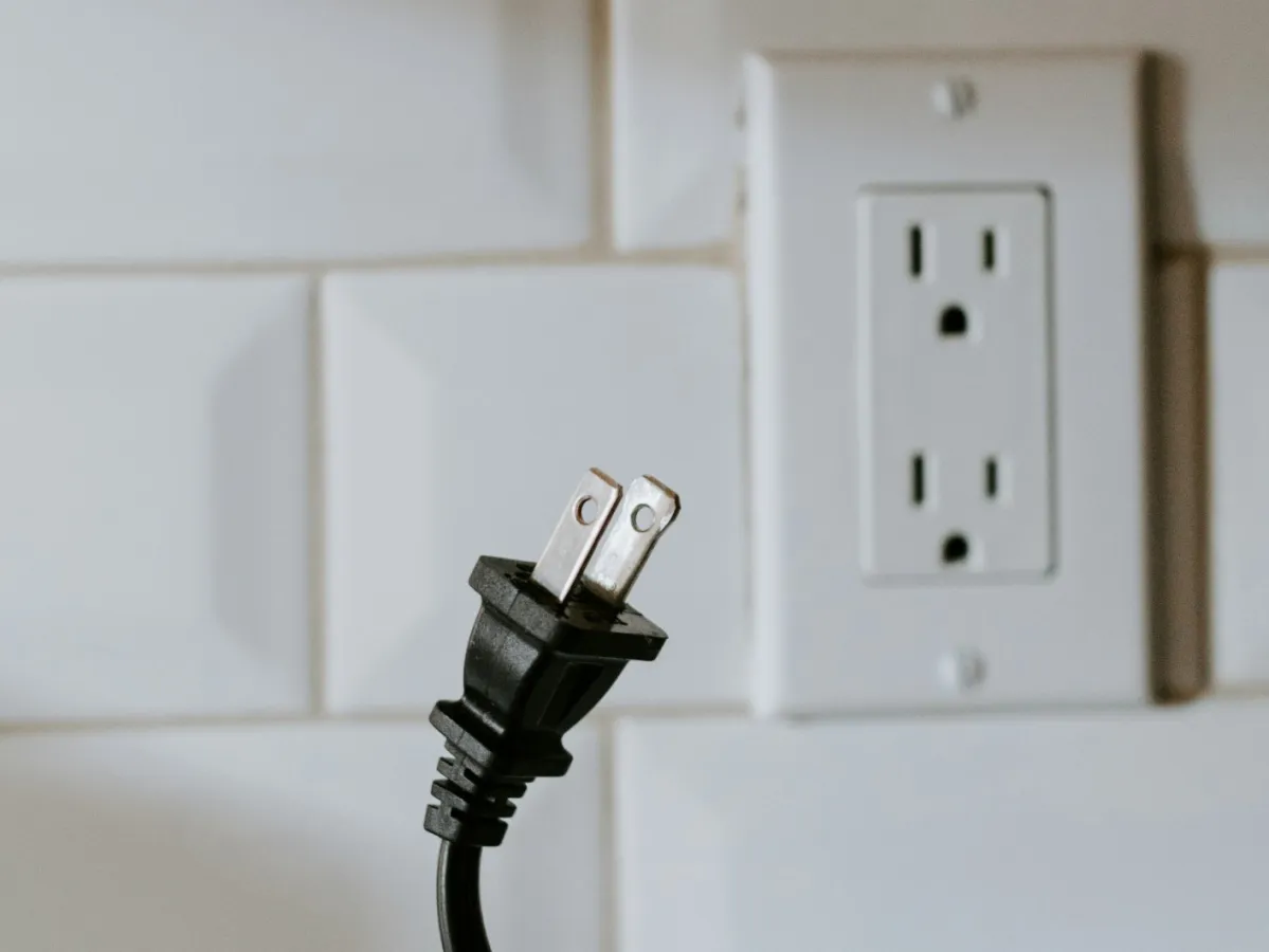 A close-up of a hand holding a power plug next to an electrical outlet on tiled wall.