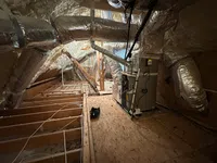 Insulated attic space with HVAC unit and ductwork wrapped in foil insulation on wooden floor framing.