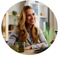 Smiling blonde woman with long hair sitting at a table during a casual meeting indoors.