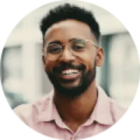 Smiling man with glasses and a beard wearing a light pink shirt in a bright indoor setting