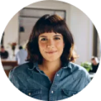 Smiling woman with short dark hair wearing denim shirt in a bright, modern indoor setting.