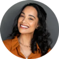 Smiling woman with curly dark hair wearing an orange shirt against a gray background