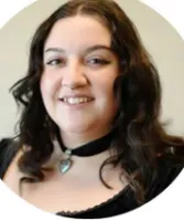 Smiling woman with curly dark hair wearing a black choker necklace with a heart pendant.