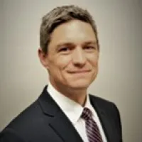 Professional man in a suit and tie smiling with a neutral background in a corporate headshot photo.