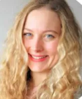 Close-up portrait of a smiling woman with curly blonde hair and blue eyes against a neutral background