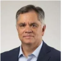 Middle-aged man with gray hair wearing a navy blazer and light blue shirt against a neutral background